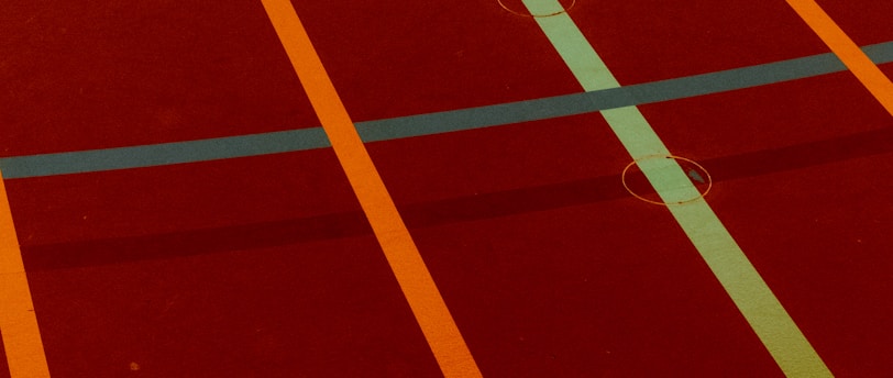 A sports court with intersecting lines in orange and blue, creating geometric patterns on a reddish-brown surface.
